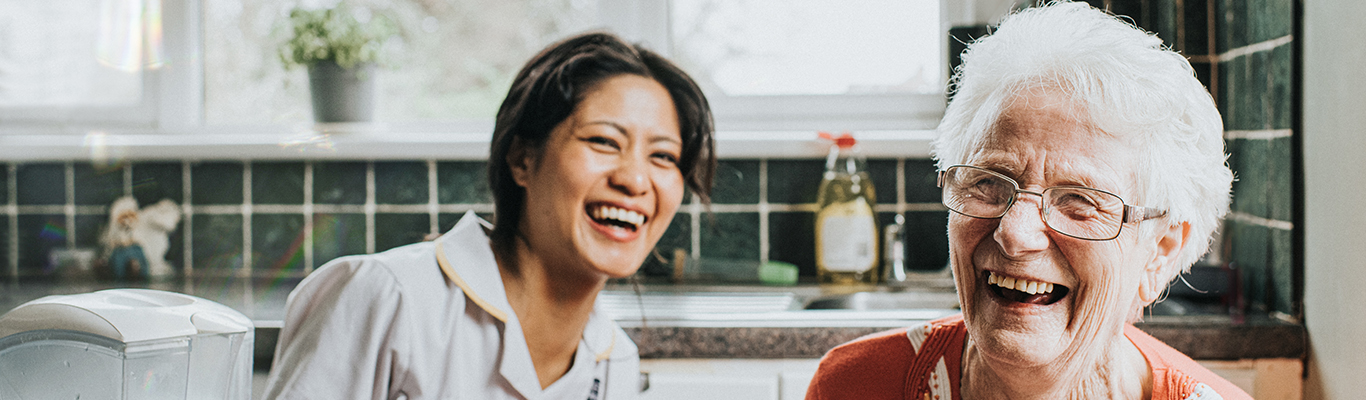 Image of a caregiver with a patient sitting in the patient's kitchen bonding and laughing